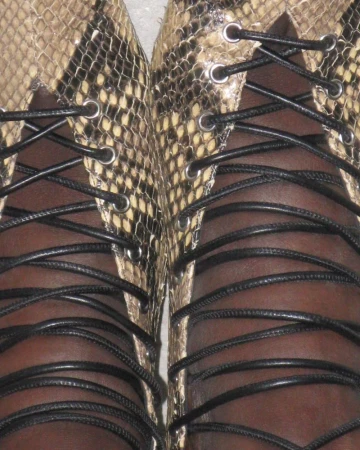 Close-up of two feet in tan and black snakeskin lace-up shoes with black laces. Focus on the shoes and shoelaces, indoors.