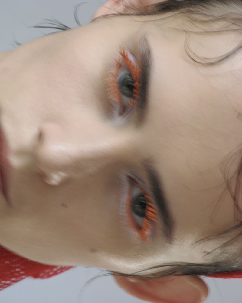 Close up beauty portrait of a model with vibrant orange mascara and styled wet hair for Dries Van Noten