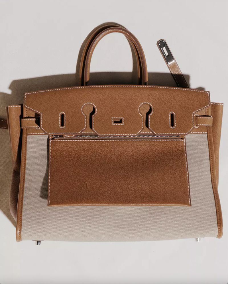 Studio shot of a Hermès Birkin handbag featuring tan leather and cream canvas, top handles, and silver hardware, presented on a light background.