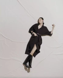 Model Chu Wong posing on a textured white backdrop wearing a black dress and boots for Hermes S/S 25