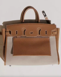 Hermes tan leather and canvas handbag with top handles displayed against a neutral background