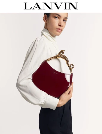 Fashion shot of a woman holding a red patent leather handbag with an animal-shaped gold handle, wearing a white top and black pants.