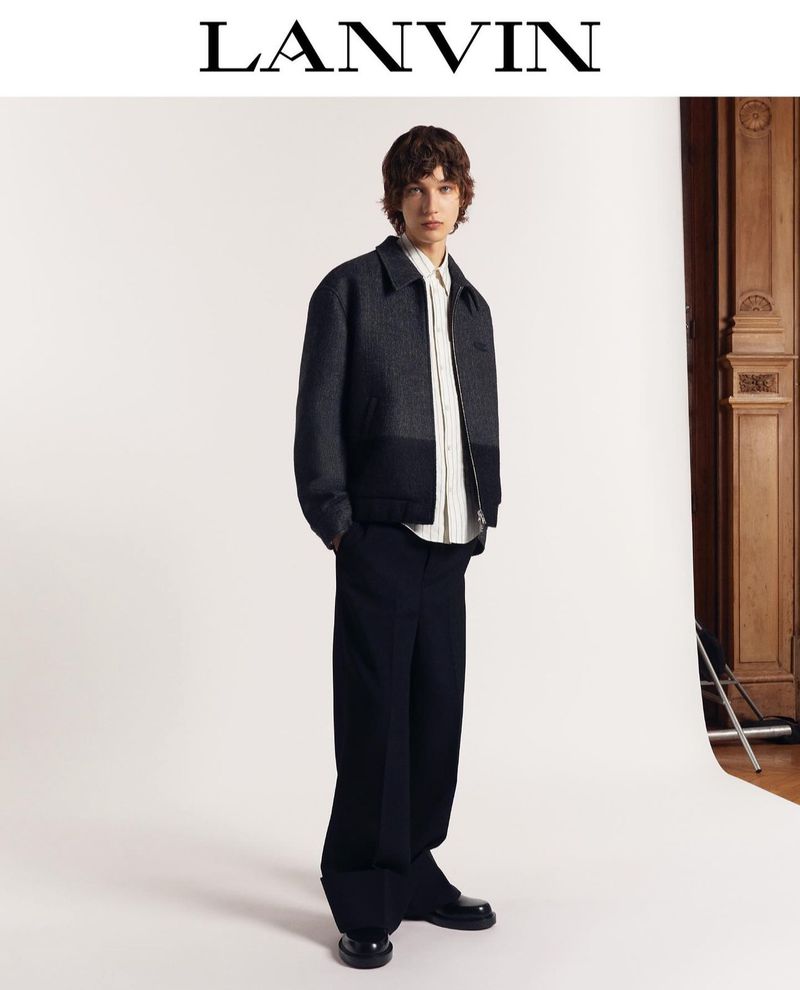 A model poses in a dark grey jacket with a white shirt and dark baggy trousers. A fashion shot for Lanvin with natural light.