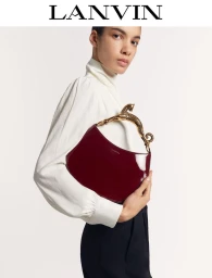 Model wearing a white blouse holding a burgundy patent handbag with a golden animal handle against a plain background