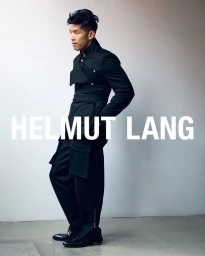 Man wearing a black structured coat and trousers against a pale background with overlaid brand text