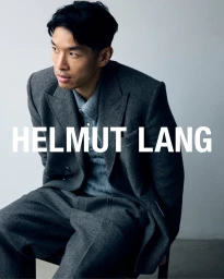 Man wearing a dark grey tailored suit jacket and matching trousers seated against a plain light grey backdrop.