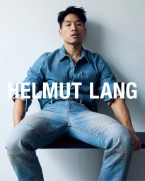 Man wearing a blue denim shirt and matching jeans seated against a plain light wall with overlaid brand text.