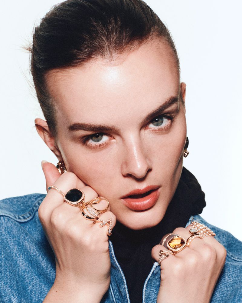Model Aylah Peterson wearing multiple gold gemstone rings and a denim jacket against a bright white background.