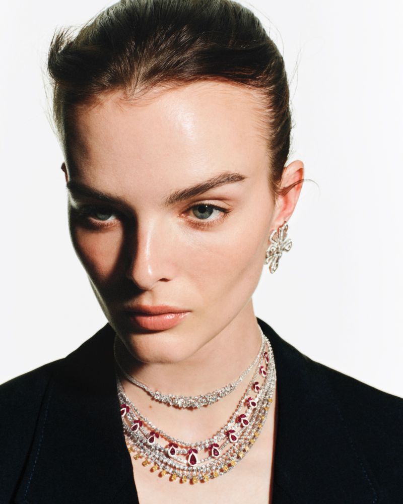 Close-up portrait of model Aylah Peterson wearing layered diamond necklaces and earrings against a white background
