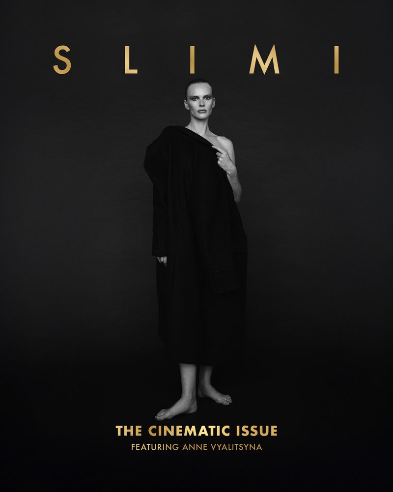 Black and white fashion magazine cover featuring a woman in a draped coat against a dark background, with gold lettering.