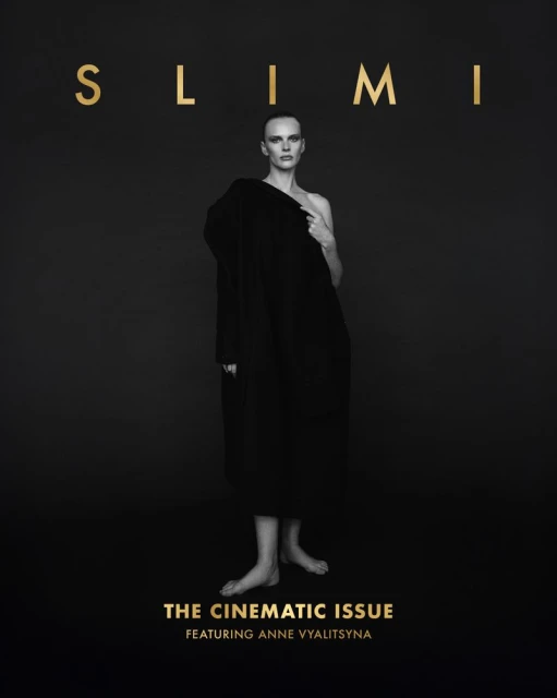 Black and white fashion magazine cover featuring a woman in a draped coat against a dark background, with gold lettering.