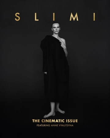 Black and white fashion magazine cover featuring a woman in a draped coat against a dark background, with gold lettering.