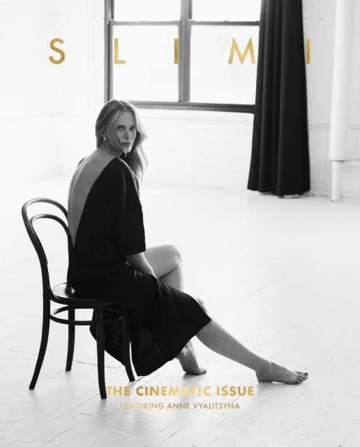 Elegant fashion shot featuring a poised blonde model in a black dress seated on a chair in a minimalist white photo studio setting.