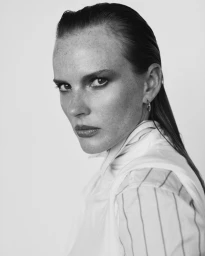 Black and white close-up portrait of model Anne Vyalitsyna with slicked-back hair, freckles, and a striped shirt against a white backdrop.