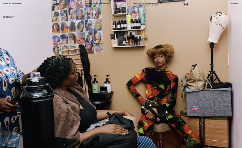Two women in a hair salon. One woman with braids sitting in a chair while another woman works on her hair, salon setting with product shelves.