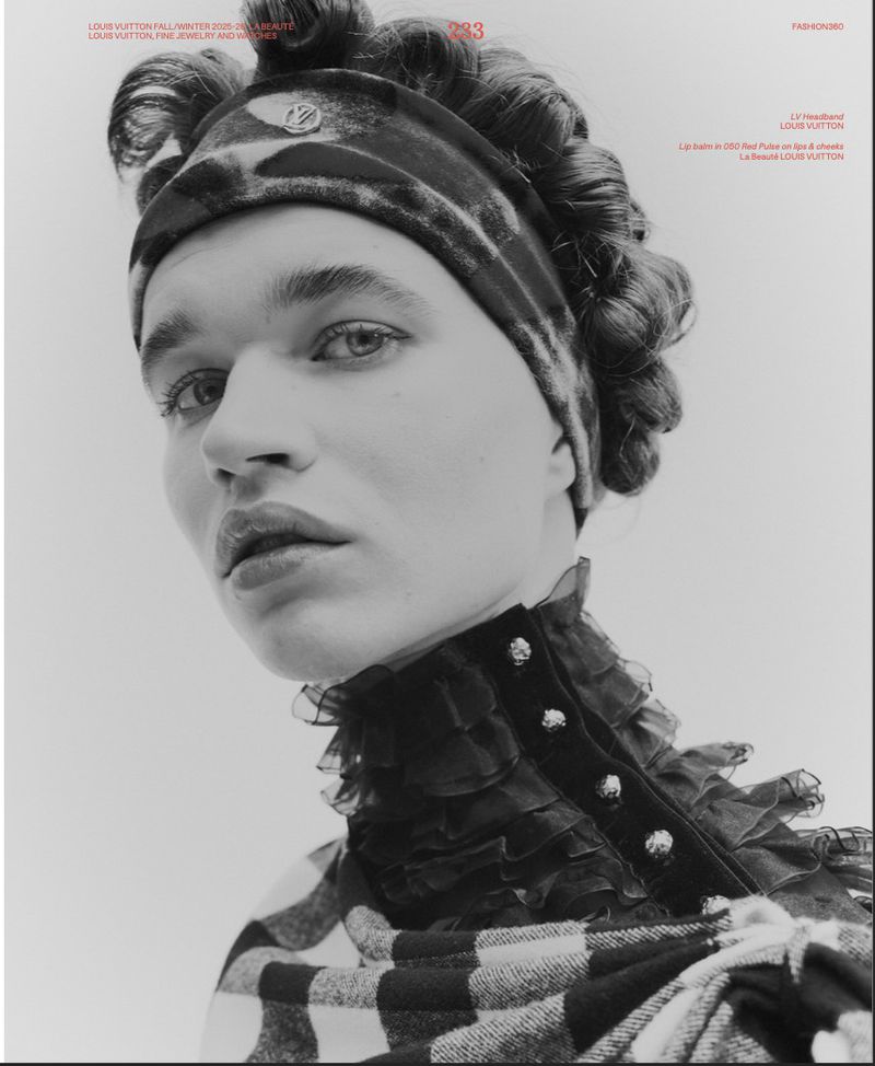 Portrait of a woman with curled hair wearing a patterned headband and a black and white checkered top with a ruffled collar.