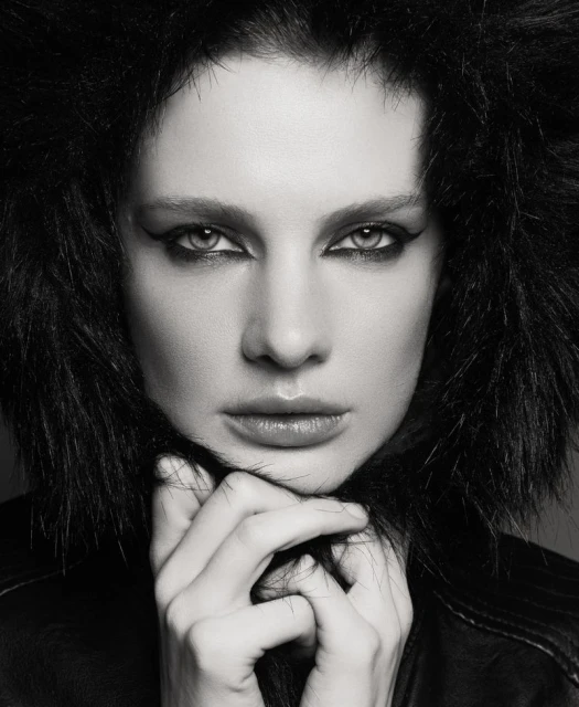 Striking black and white portrait of a woman with dark hair, dramatic eye makeup, and black leather jacket. Hands are seen near her neck.