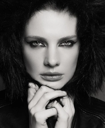 Striking black and white portrait of a woman with dark hair, dramatic eye makeup, and black leather jacket. Hands are seen near her neck.