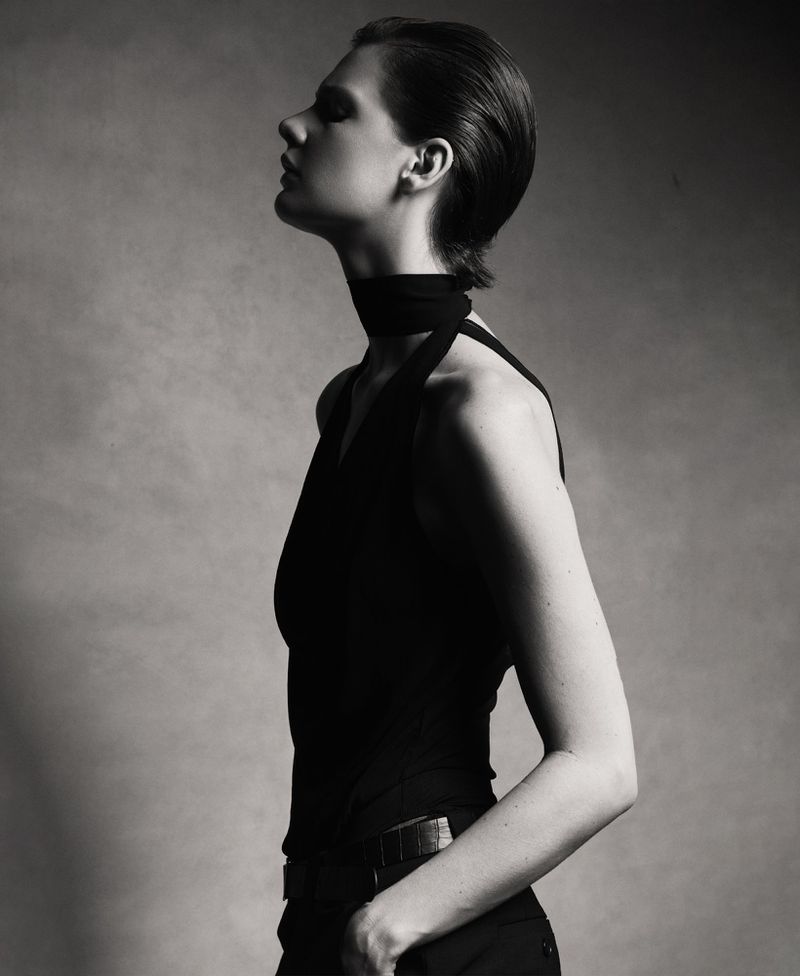 Monochrome portrait of a female fashion model in a sleeveless top, head tilted back, in a studio setting with soft lighting.