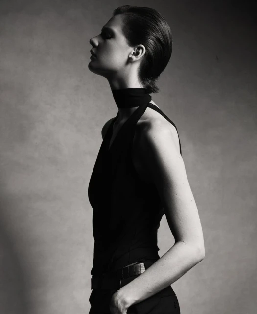Monochrome portrait of a female fashion model in a sleeveless top, head tilted back, in a studio setting with soft lighting.
