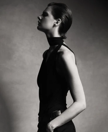 Monochrome portrait of a female fashion model in a sleeveless top, head tilted back, in a studio setting with soft lighting.