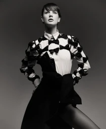 Model Mirthe Dijkstra wearing a white shirt embellished with black bows and a dark wrap skirt against a smooth grey studio backdrop.
