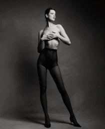 Model Mirthe Dijkstra posing in black tights, high-waisted briefs, and heels against a dark studio backdrop in black and white.