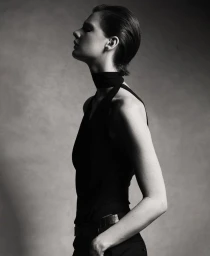 Black and white profile portrait of model Mirthe Dijkstra wearing a sleeveless black halter top and neckband against a studio backdrop.