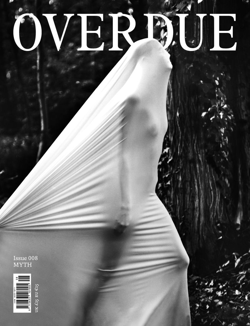 Monochrome fashion magazine cover featuring person draped in white fabric against a blurred forest backdrop, with bold, stylized text.