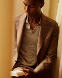 Carlos Galobart wearing a textured brown linen suit and knit polo while looking down holding a small book.