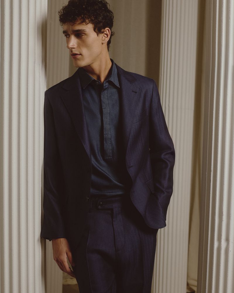 Young man in navy suit poses indoors near columns. Classic menswear fashion shot with elegant, timeless style and soft lighting.