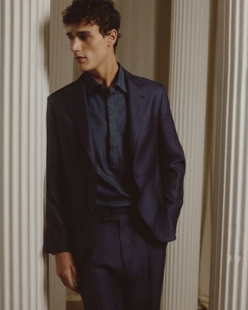 Young man in navy suit poses indoors near columns. Classic menswear fashion shot with elegant, timeless style and soft lighting.