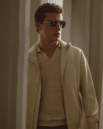 Model Carlos Galobart wears a cream hooded jacket, textured knit polo, and sunglasses for Brett Johnson Spring 2026.