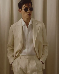 Man wearing a cream pinstripe suit and sunglasses against a draped curtain background for Brett Johnson Spring 2026 Presentation