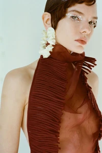 Portrait of a woman wearing a pleated burgundy halter top and large white earrings against a white background