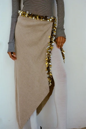 Model wearing a grey long-sleeve top and wrapped beige skirt with metallic sequin trim against white background