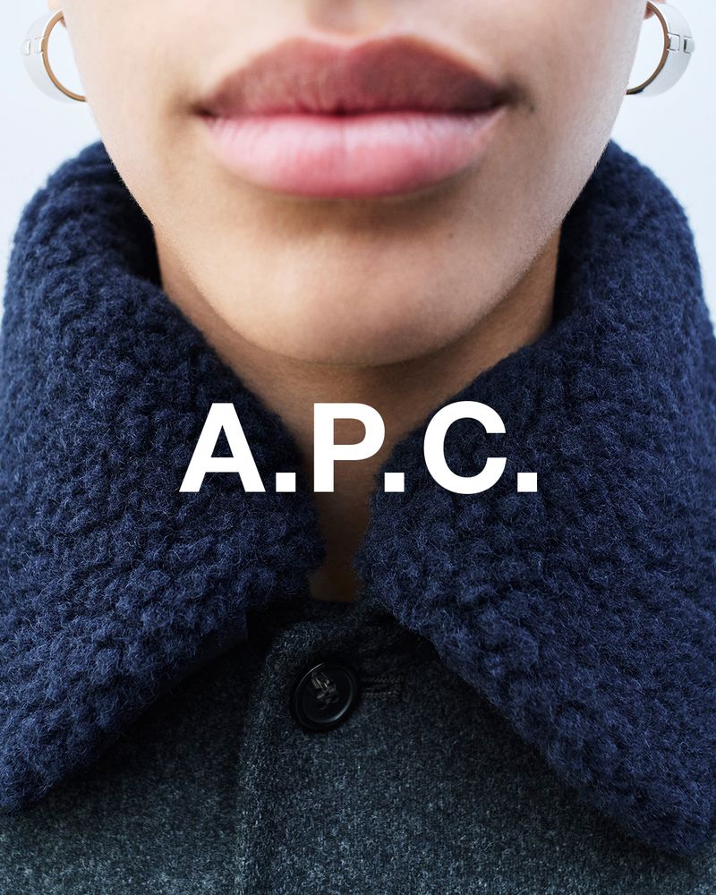 Fashion closeup featuring a woman wearing a grey wool coat with a blue sherpa collar, accessorized with hoop earrings and A.P.C logo.