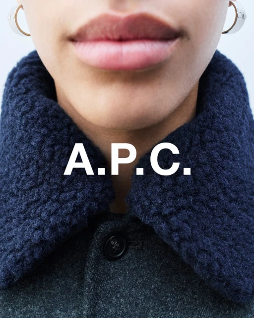 Fashion closeup featuring a woman wearing a grey wool coat with a blue sherpa collar, accessorized with hoop earrings and A.P.C logo.