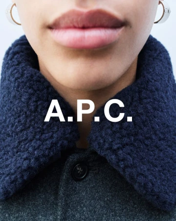 Fashion closeup featuring a woman wearing a grey wool coat with a blue sherpa collar, accessorized with hoop earrings and A.P.C logo.
