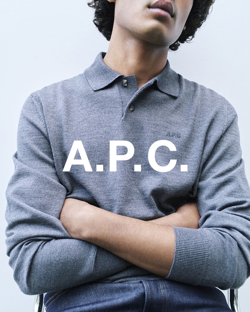 Close-up shot of an adult male wearing a gray long-sleeved polo shirt and blue jeans, sitting against a plain background. Fashion shoot.