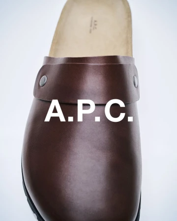 Close-up studio shot of a brown leather clog with a thick band and metal hardware, featuring the 'A.P.C.' brand logo in white.