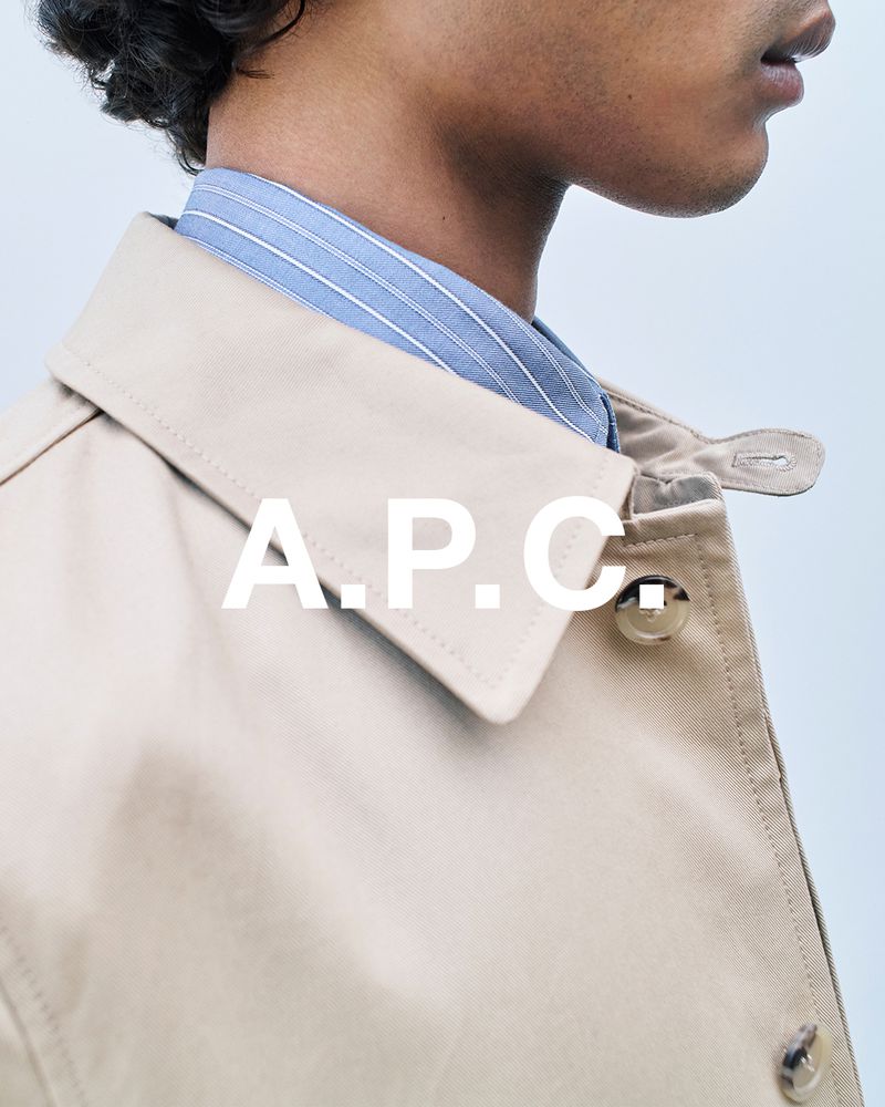 Tan trench coat detail featuring a stylish collar, button closure, and subtle blue striped shirt underneath, creating a fashionable layered look.