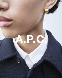 Close-up portrait of a model wearing a dark navy jacket over a white collared shirt with gold hoop earrings for A.P.C.