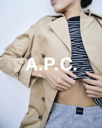 Close-up of a model wearing a beige trench coat, black and white striped top, and grey sweatpants against a white background.