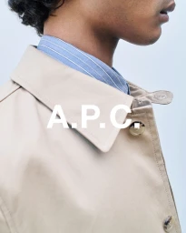 Close-up portrait of a man wearing a beige coat over a blue striped shirt against a plain light background