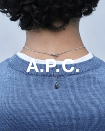 Close-up back view of a person wearing a blue sweater and a delicate silver necklace with a pendant for A.P.C.