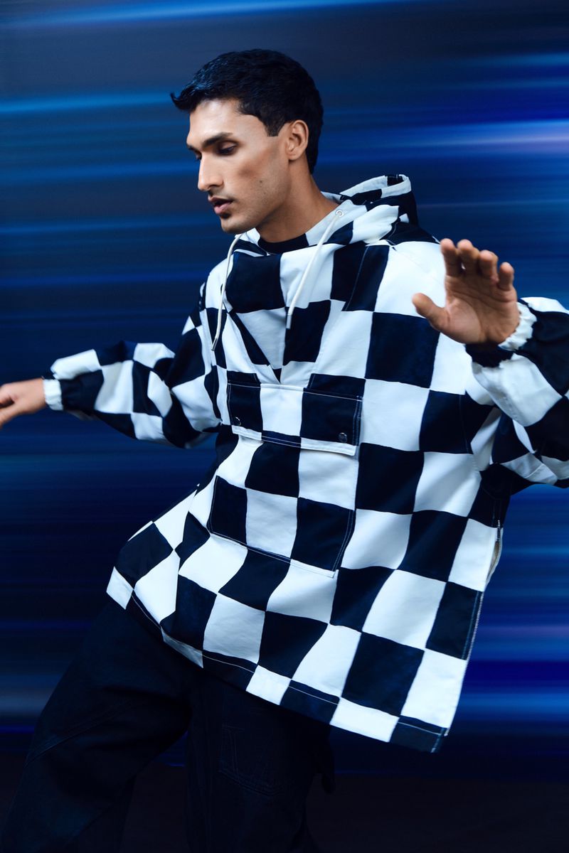 Man wearing a black and white checkered hoodie against a blurred blue motion background for Harvey Nichols