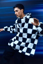 Man wearing a black and white checkered hoodie against a blurred blue motion background for Harvey Nichols