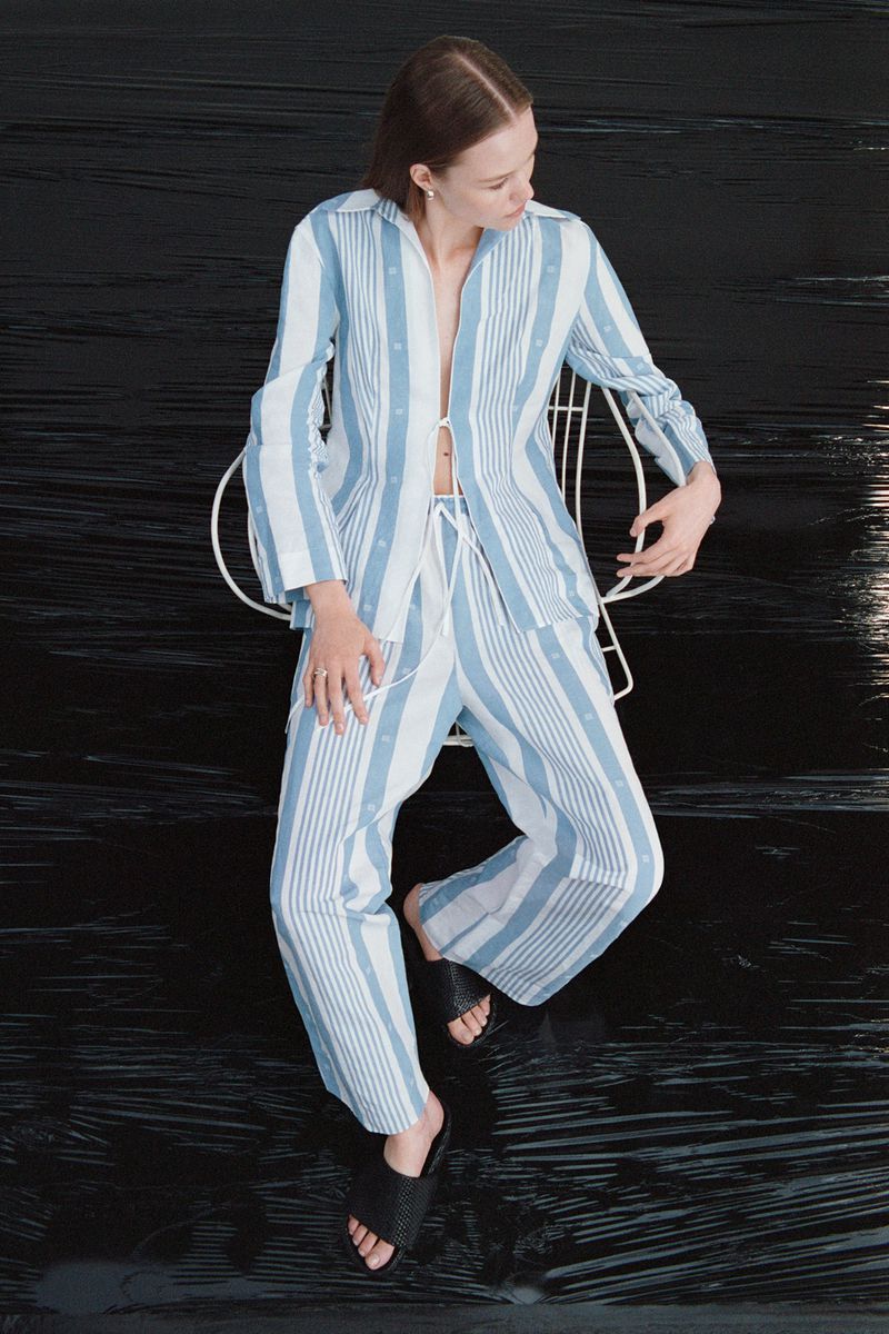 Woman in striped pajama set sitting in a white chair against a black backdrop, casual fashion portrait, comfortable clothing, indoor studio shot.