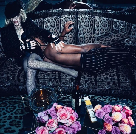 Madonna and a male model pose intimately on a leopard print couch, showcasing high fashion and intimate aesthetics in a studio setting.